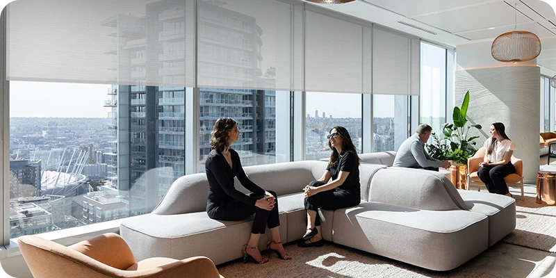 Modern living room with motorized blinds, large windows and a cityscape view, featuring people sitting on a sofa