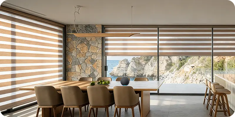 Modern dining area with Yoolax motorized blinds overlooking a scenic coastal view